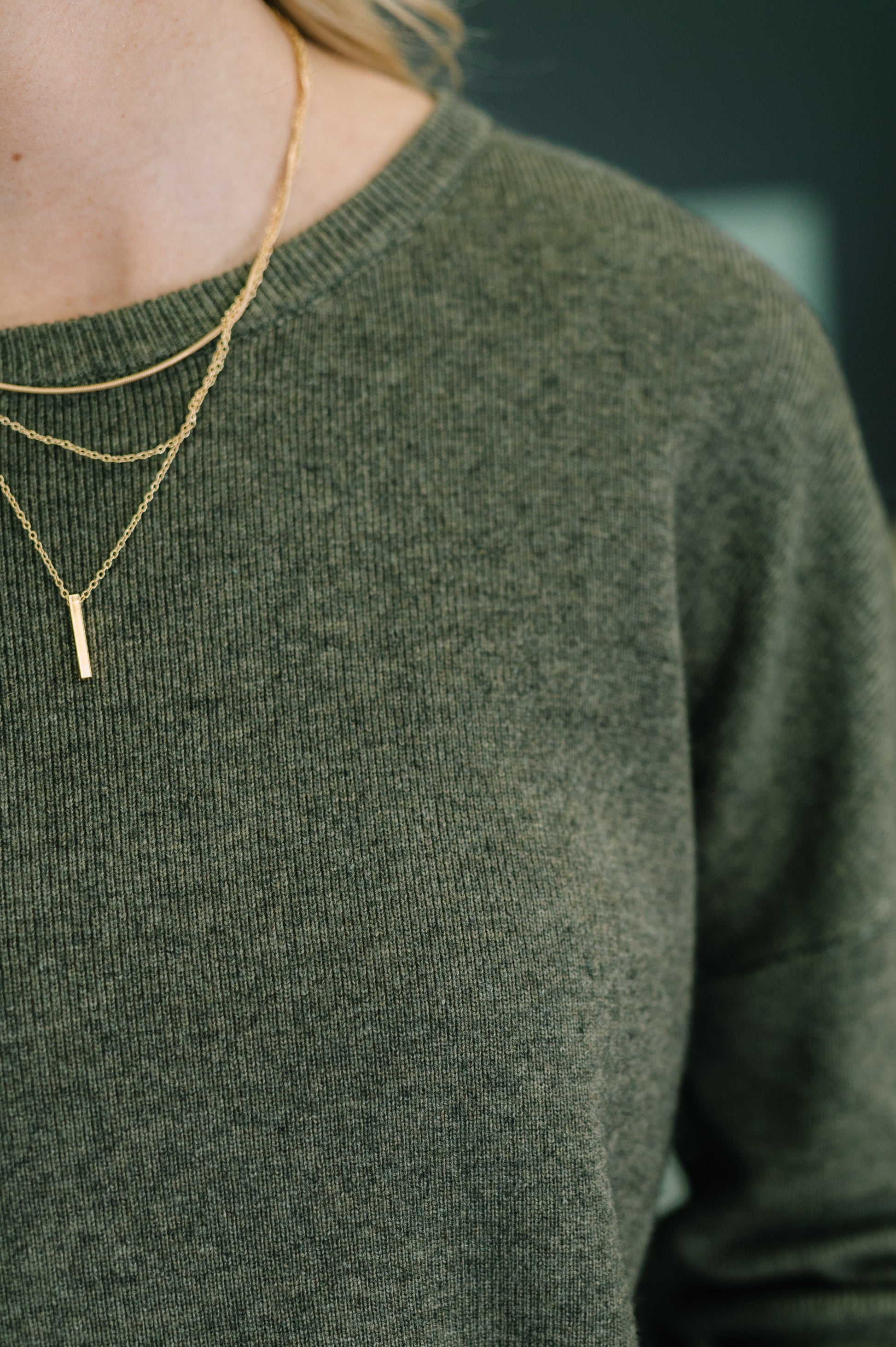 Person wearing a green sweater with a gold necklace