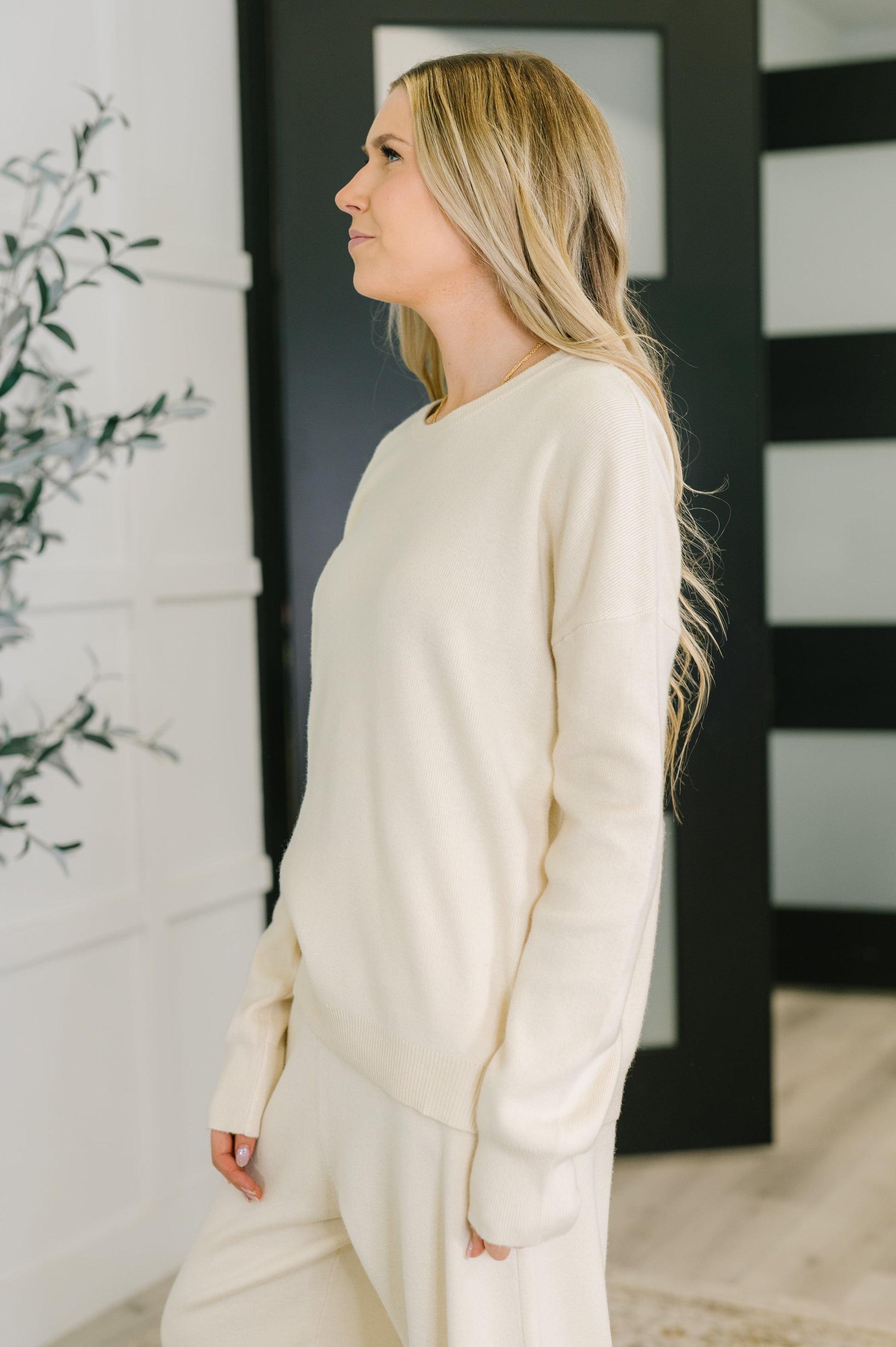 Woman wearing a cream-colored sweater and pants in a minimalistic room.