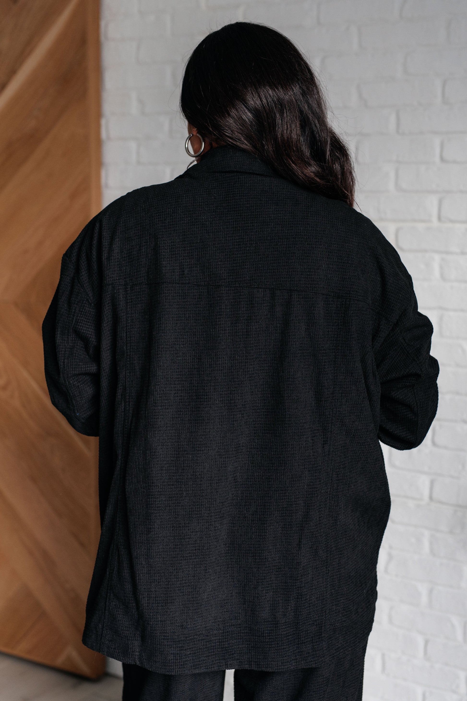 Person wearing a black jacket standing against a white brick wall.