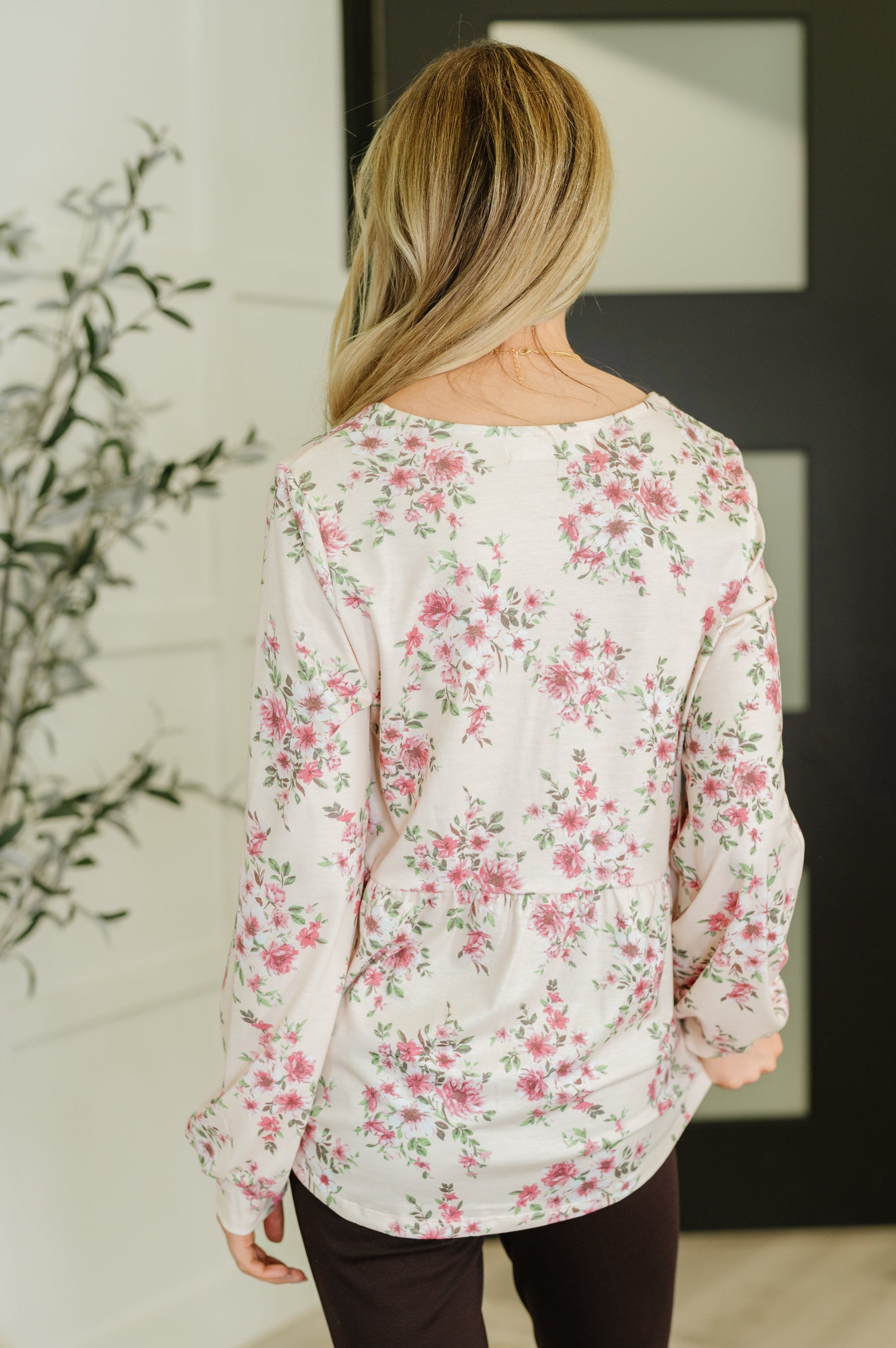 Person wearing a floral blouse in a room with a plant and framed picture.
