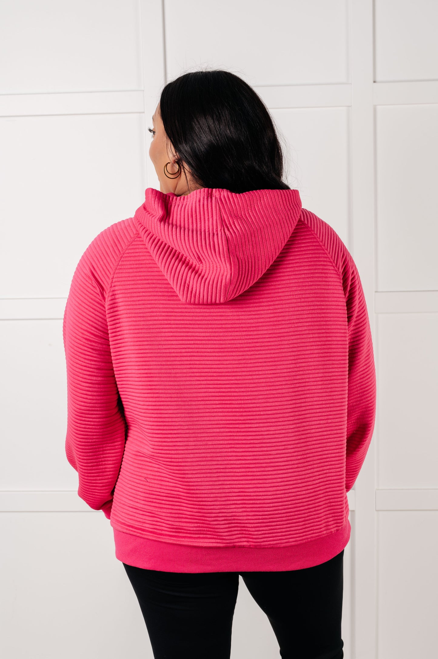 Person wearing a pink textured hoodie against a white tiled wall