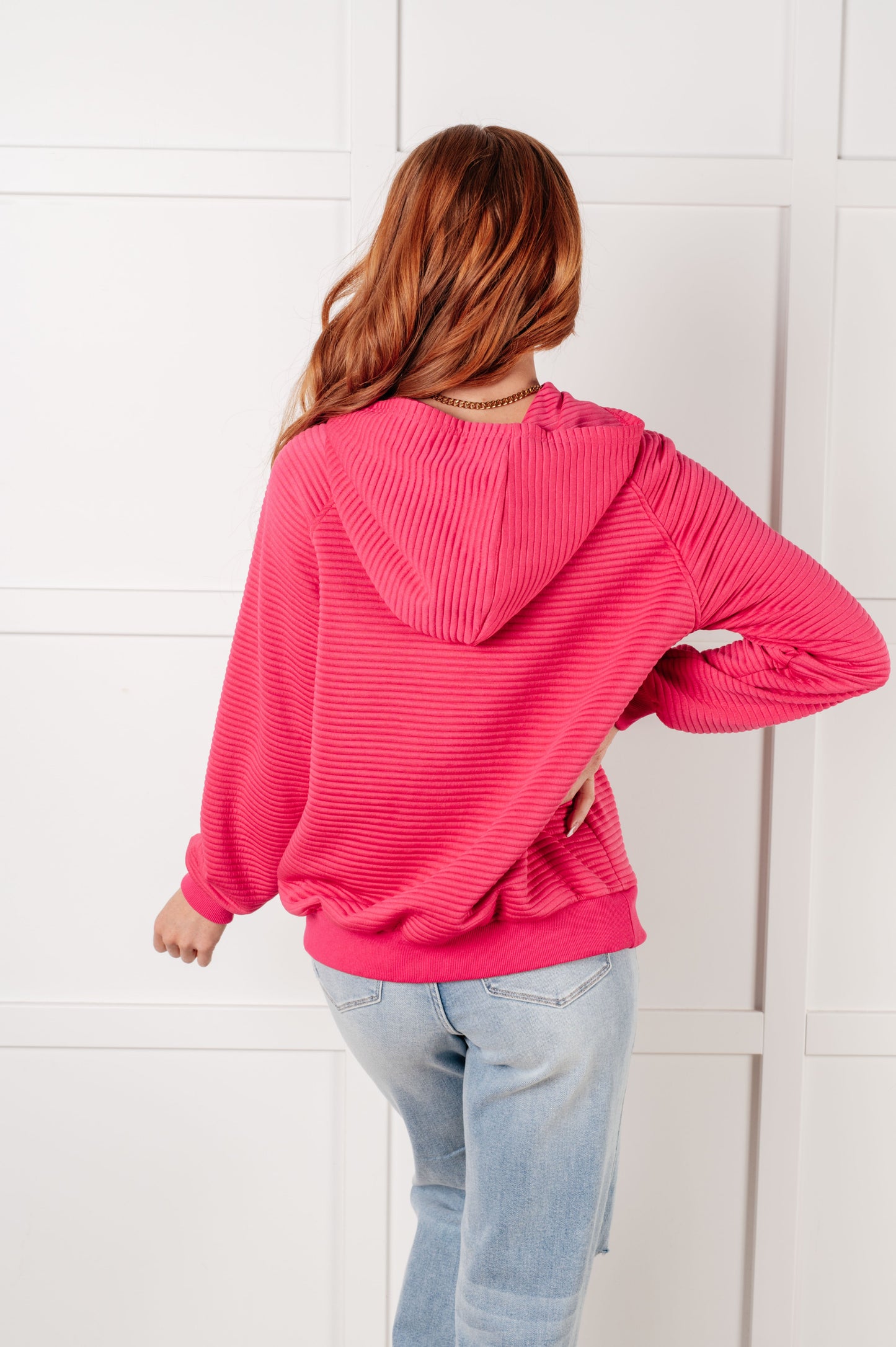Person wearing a pink hoodie and light blue jeans against a white wall
