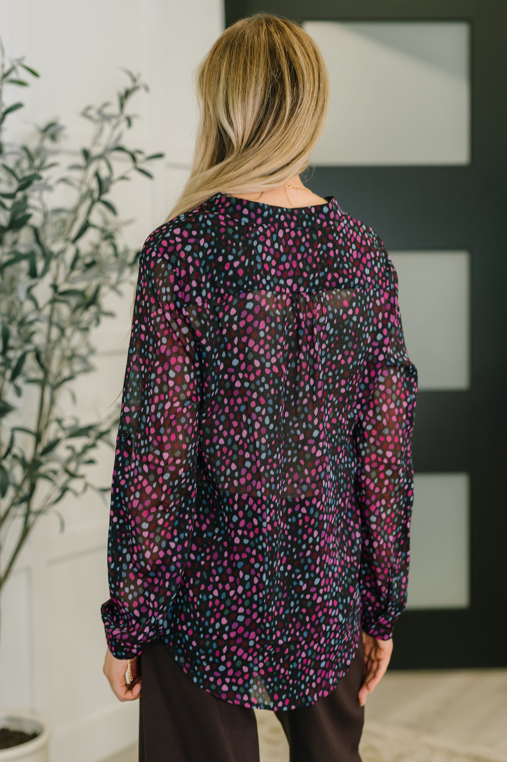Person wearing a long-sleeve, patterned blouse in a room with a plant and abstract wall art.