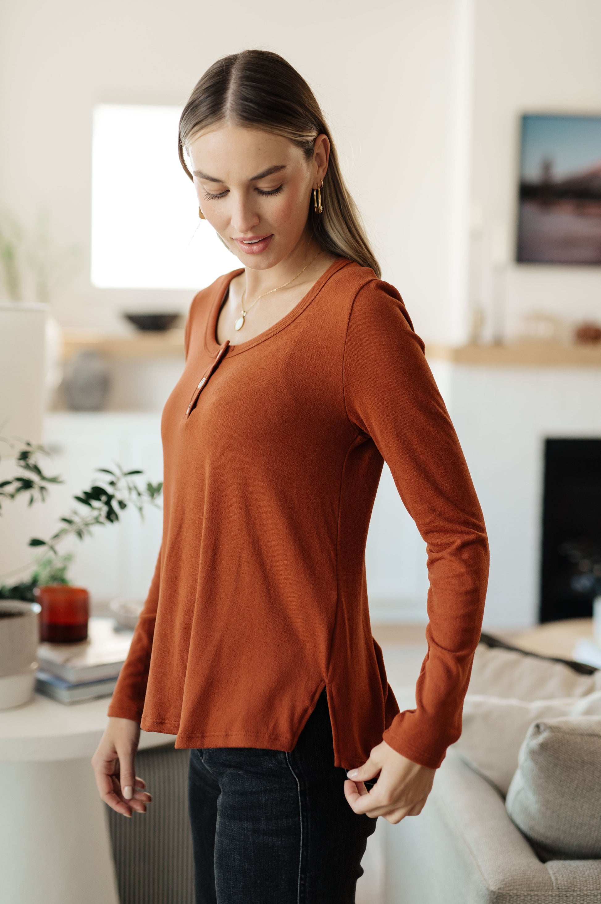 Woman wearing a rust-colored long-sleeve top in a living room setting