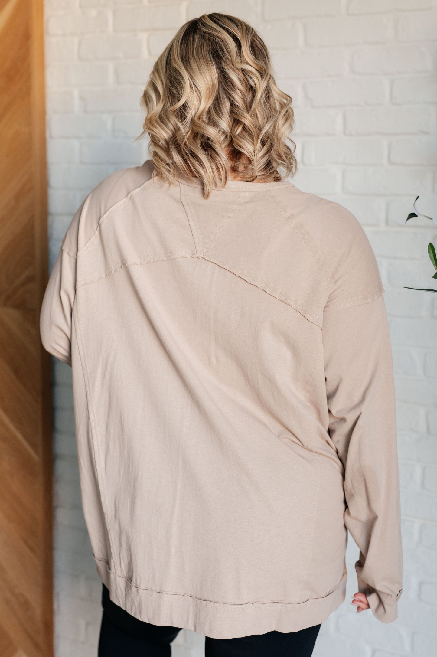Person wearing a beige jacket in front of a white brick wall