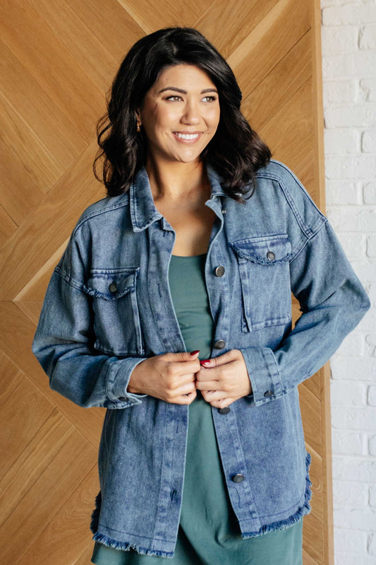 Woman wearing a denim jacket standing against a wooden paneled wall.
