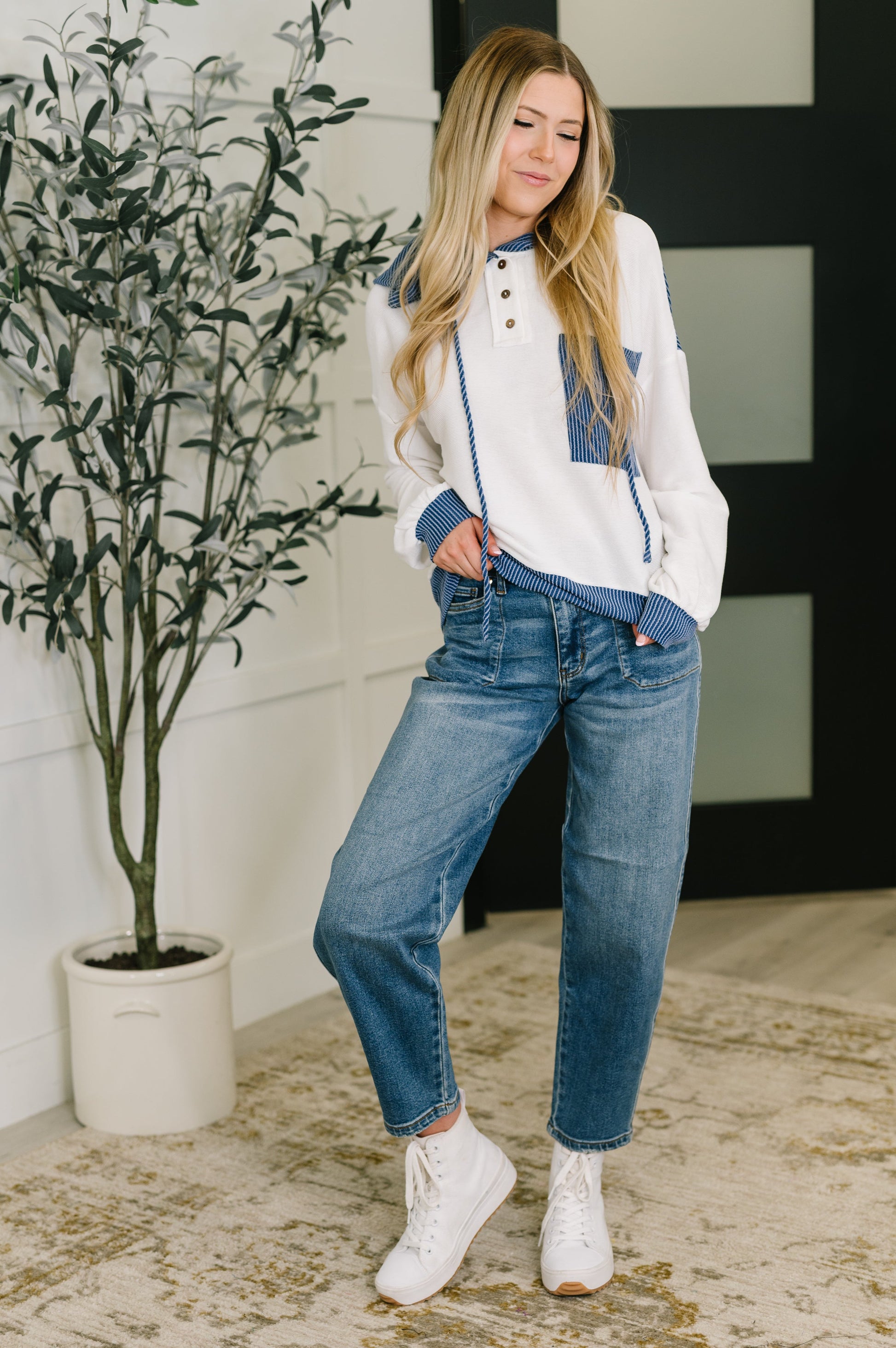 Woman wearing a white hoodie with blue accents and jeans, standing indoors.