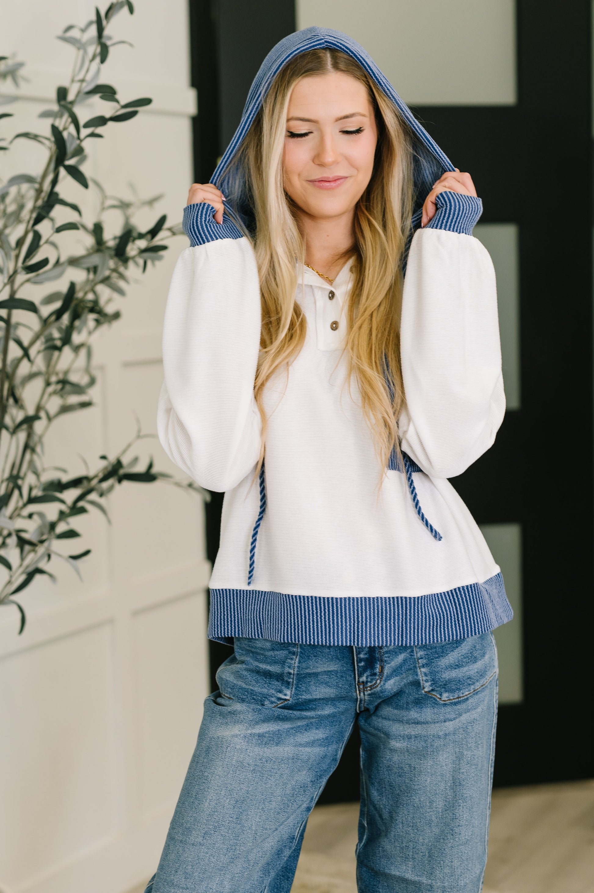 Woman wearing a white hoodie with blue accents and jeans, standing indoors.