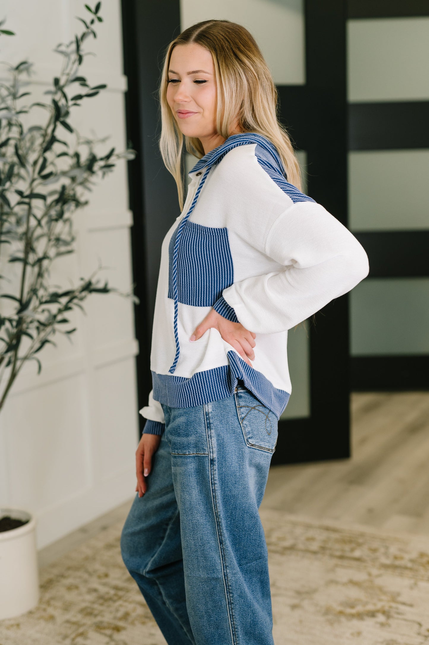 Woman wearing a white hoodie with blue accents and jeans, standing indoors.