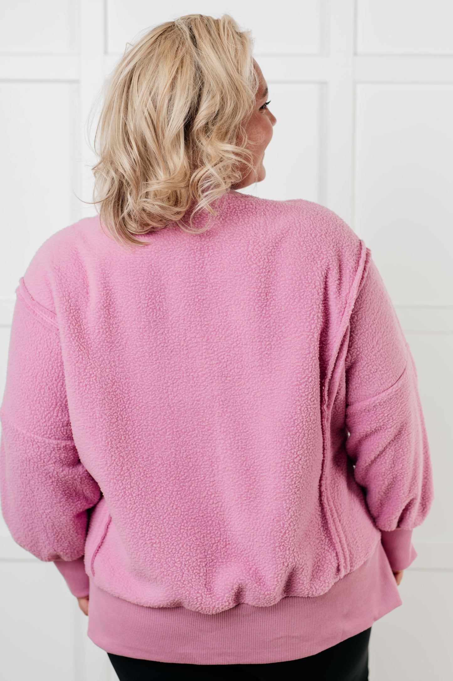 Person wearing a pink fleece sweater against a white tiled wall