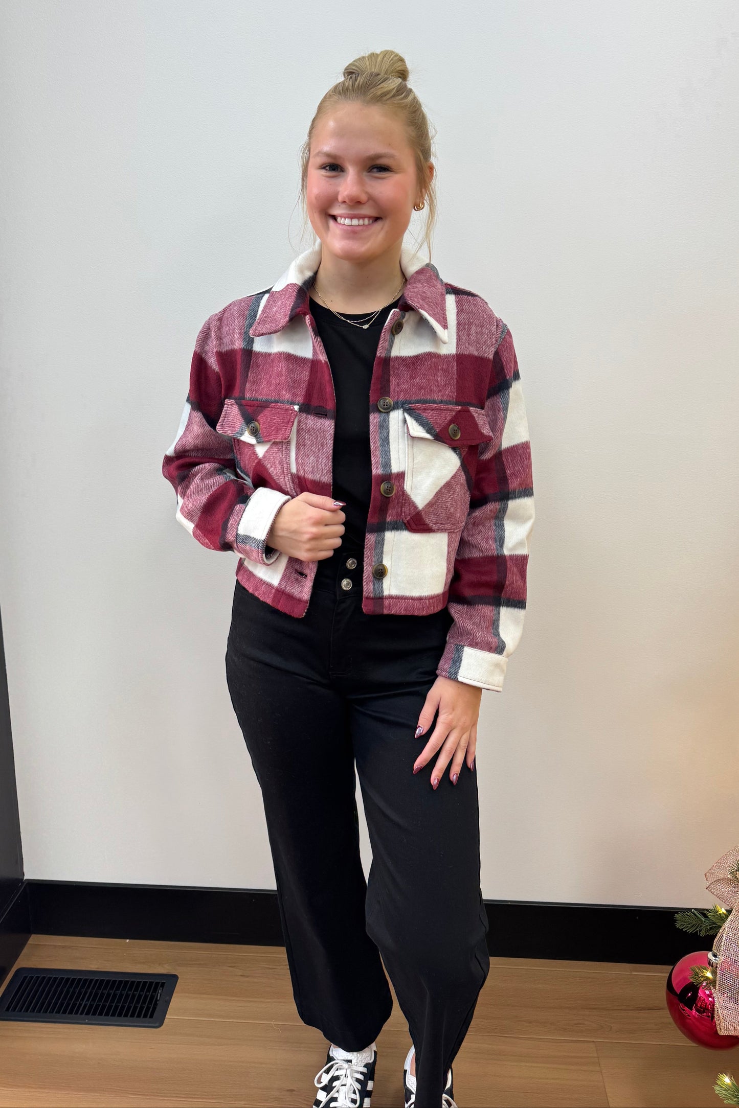 Person wearing a plaid shirt and black pants standing in front of a white wall.