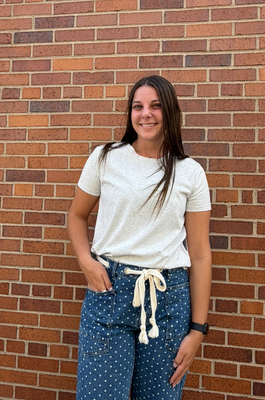 A woman stands in front of a red brick wall wearing a white short-sleeve t-shirt and blue polka-dot drawstring pants.