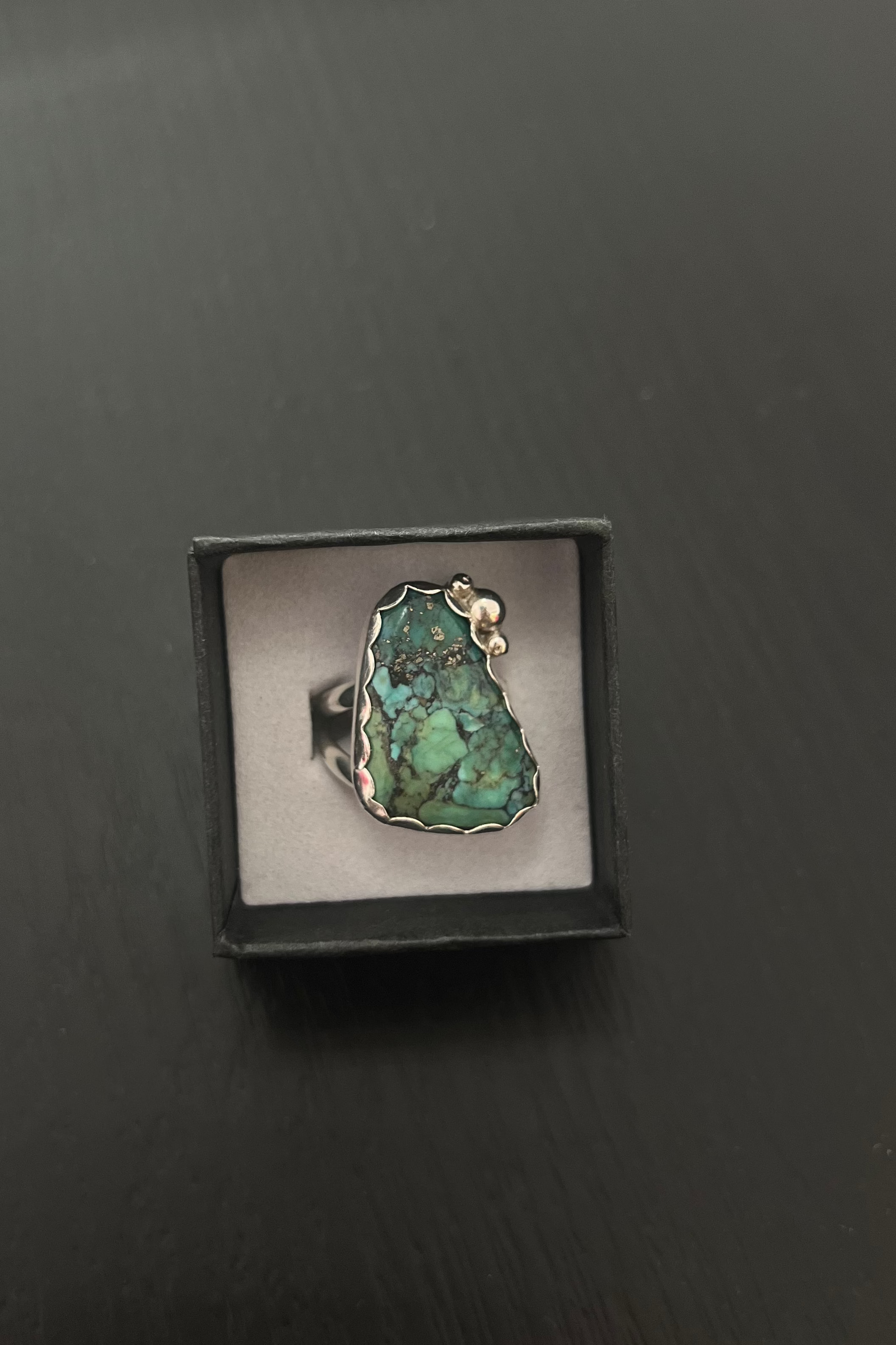 Ring with a green stone in a black box on a dark surface