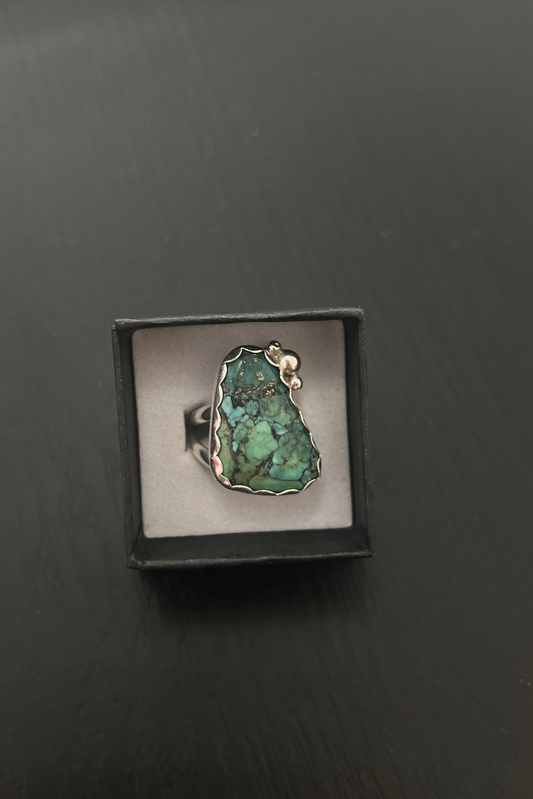 Ring with a green stone in a black box on a dark surface