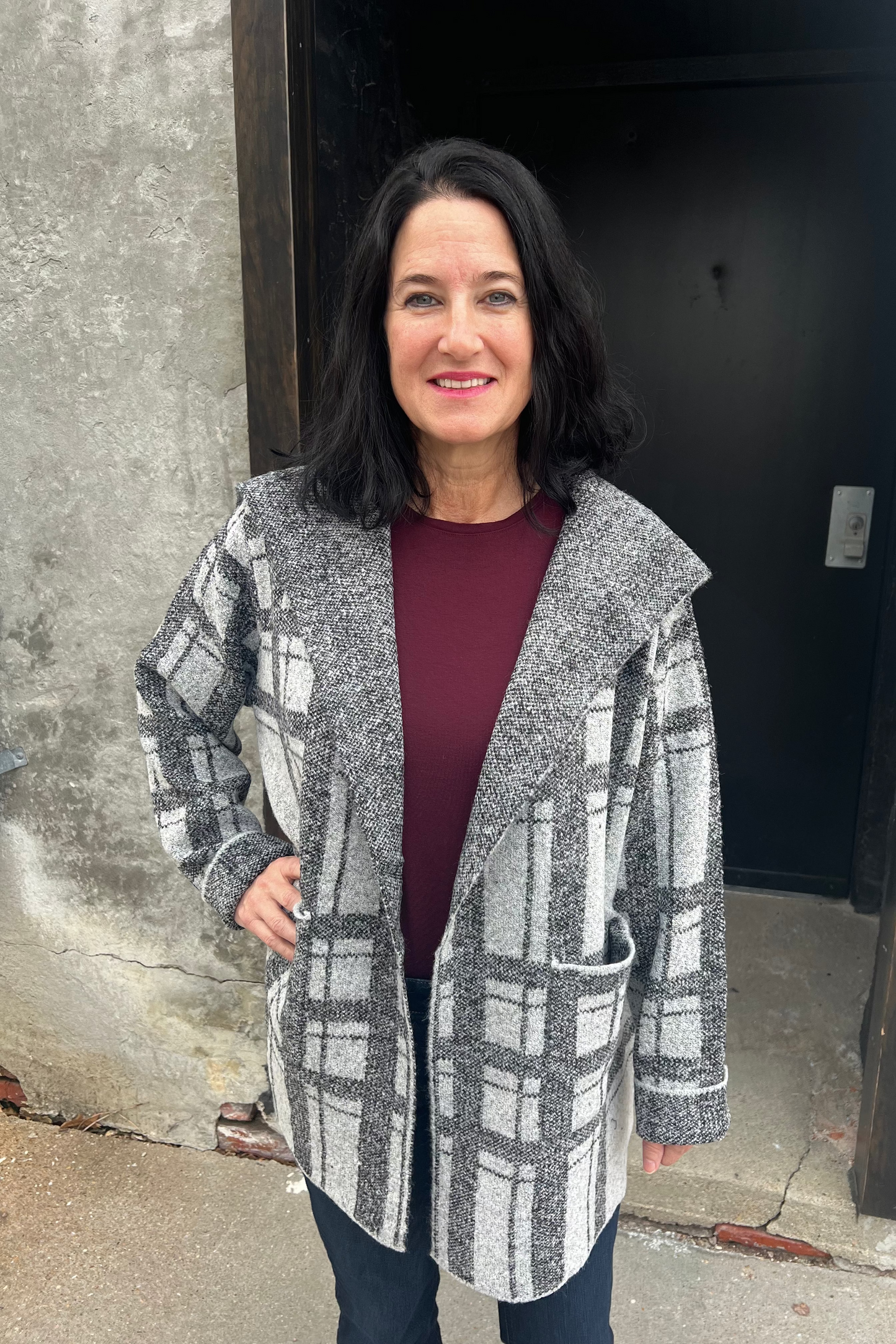 Woman wearing a plaid coat standing against a wall.