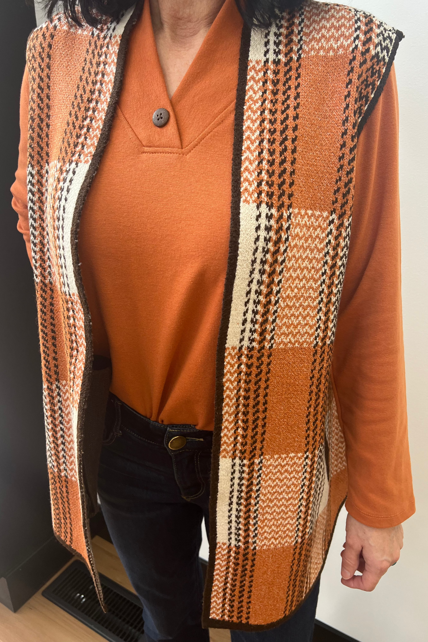 Person wearing a patterned vest over an orange shirt with a neutral background
