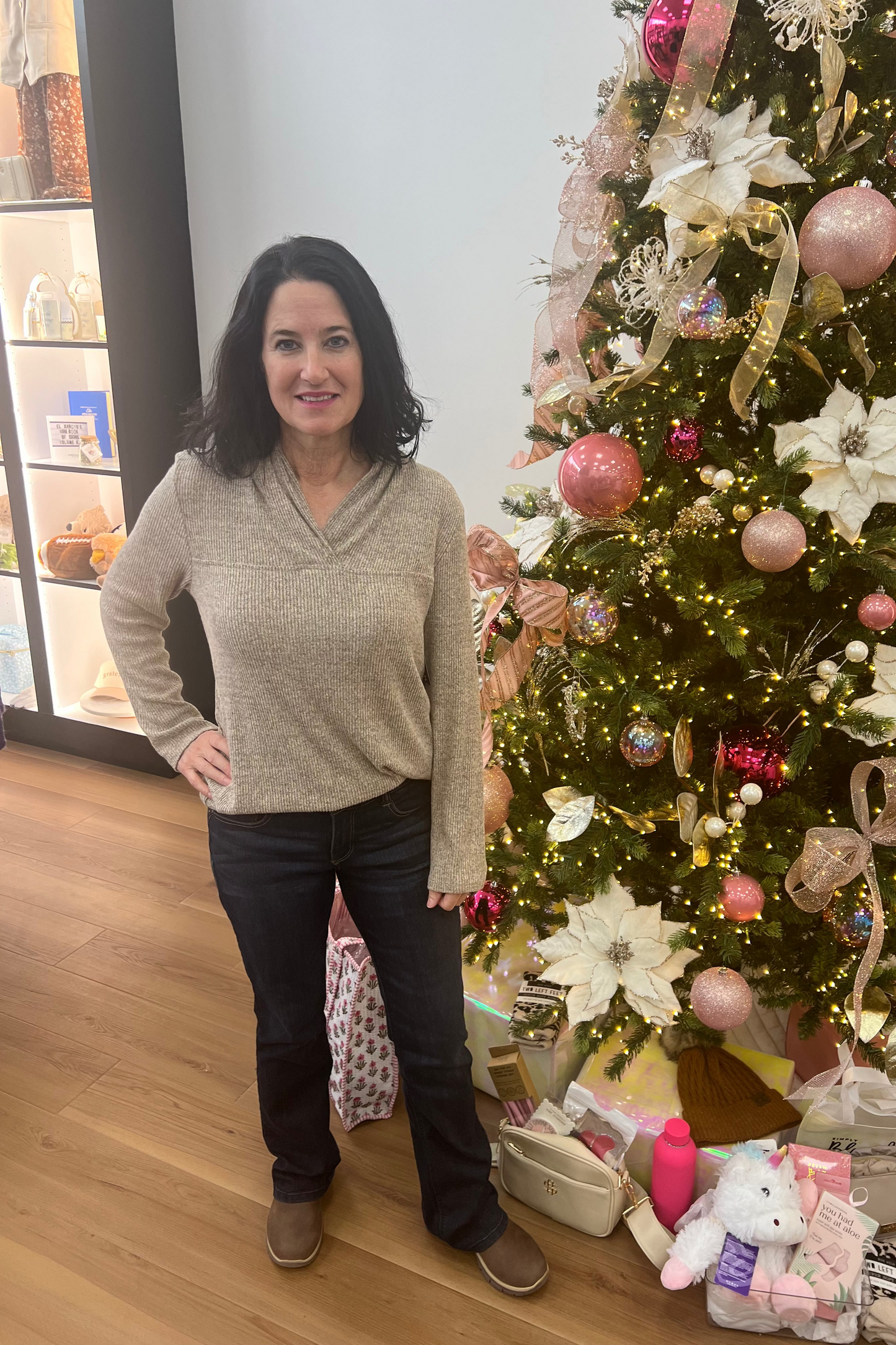 Woman standing next to a decorated Christmas tree with presents underneath.