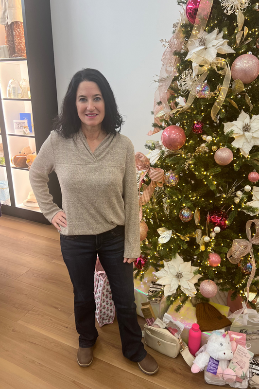 Woman standing next to a decorated Christmas tree with presents underneath.