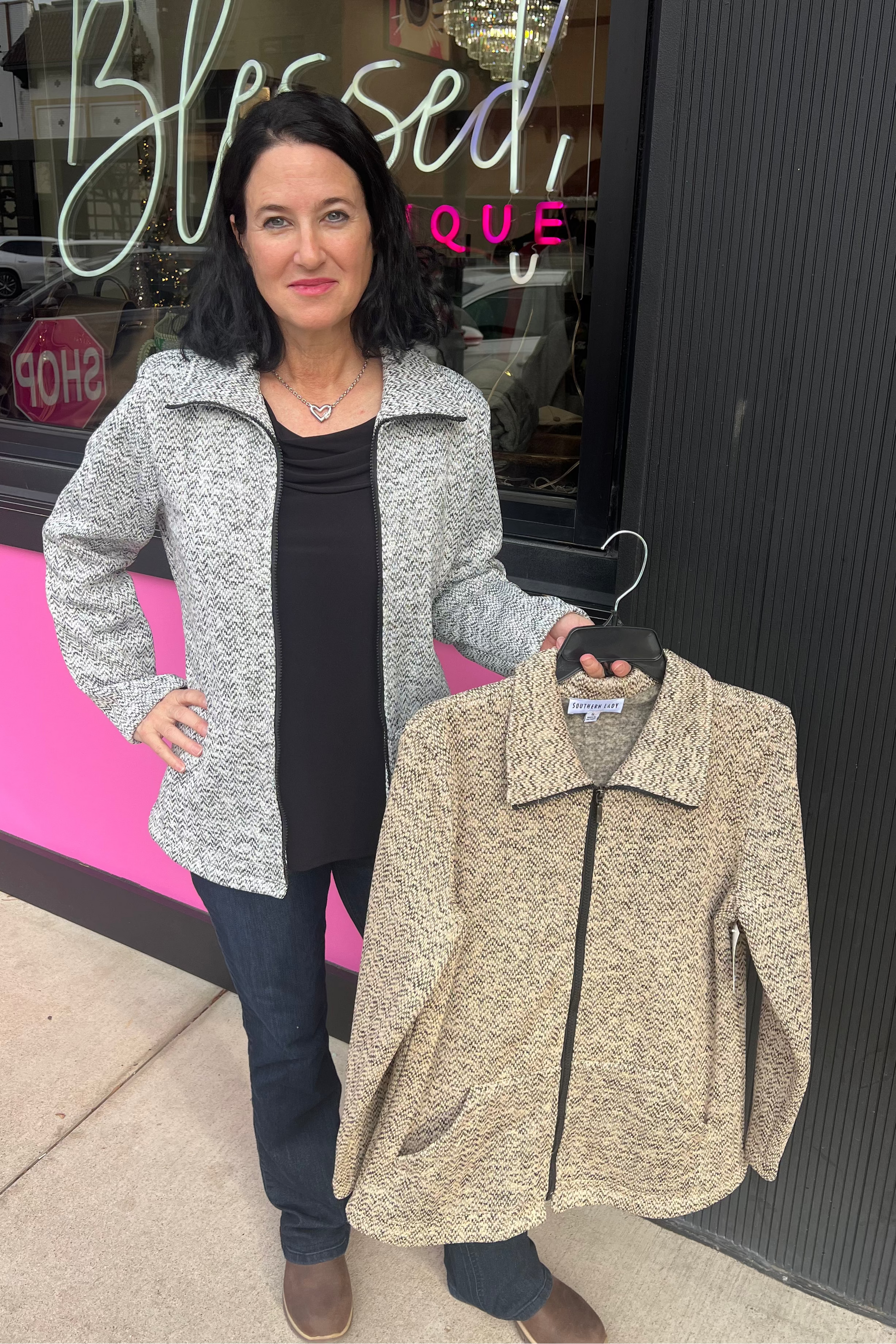 Woman holding a beige jacket in front of a store with 'Simply Blessed' sign.
