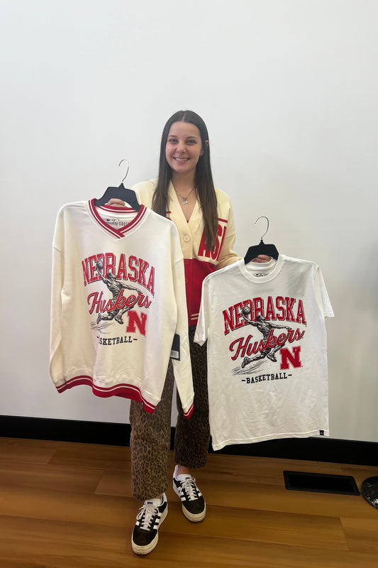 Person standing next to a table with multiple 'Nebraska' branded bags on a white background
