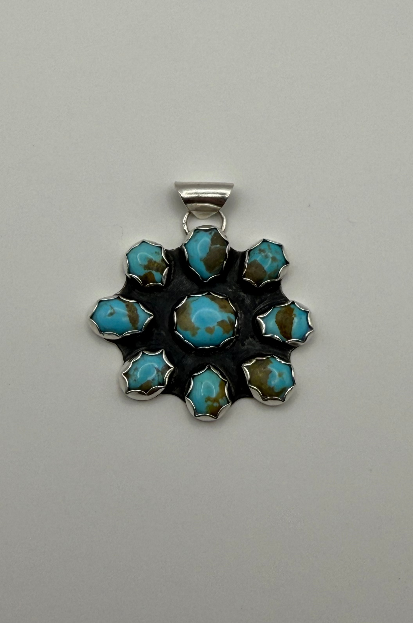 A silver pendant featuring a floral arrangement of turquoise stones with brown matrix, set against a plain light gray background.