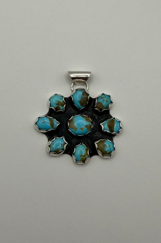 A silver pendant featuring a floral arrangement of turquoise stones with brown matrix, set against a plain light gray background.