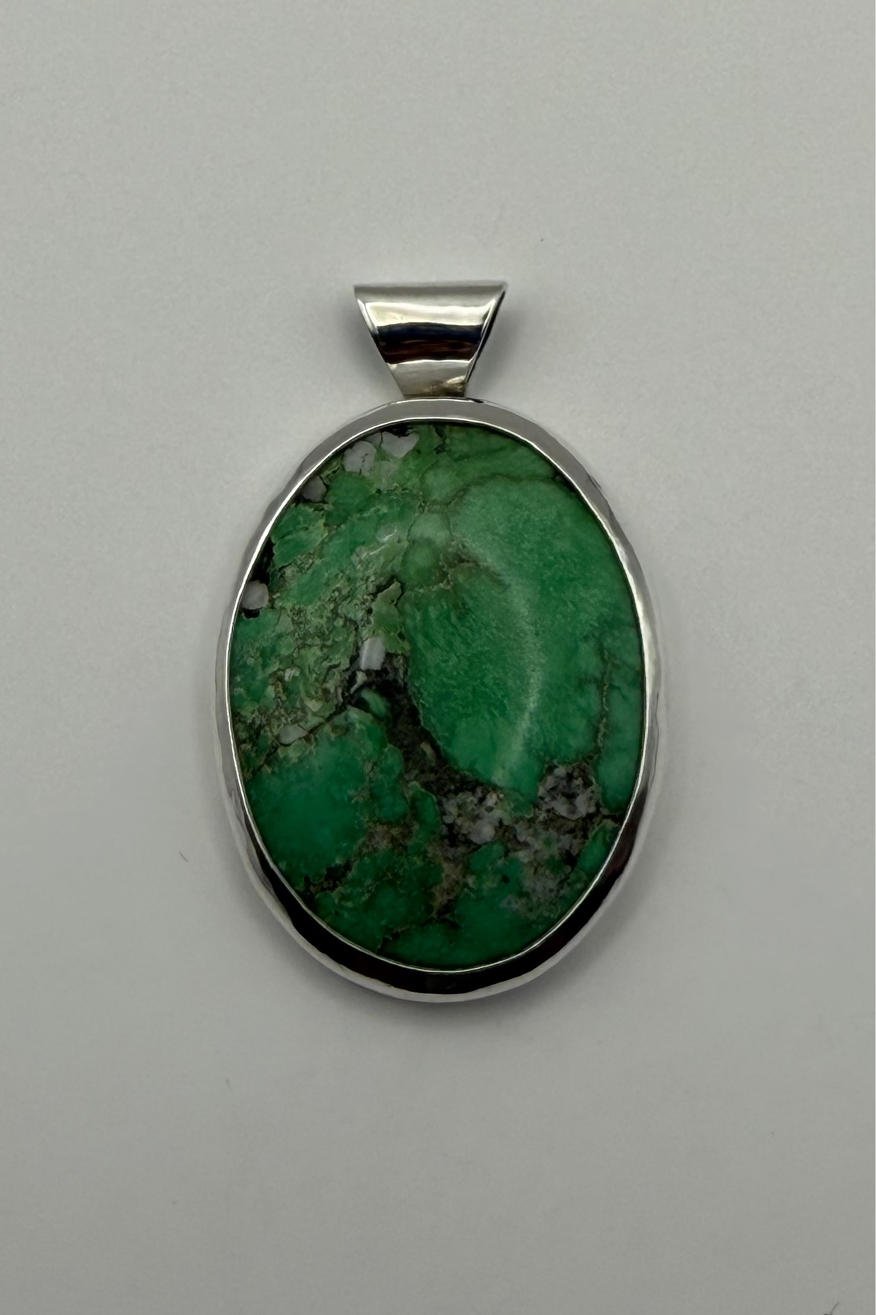 A green stone pendant, set in a polished sterling silver bezel with a bail, shown on a white background.