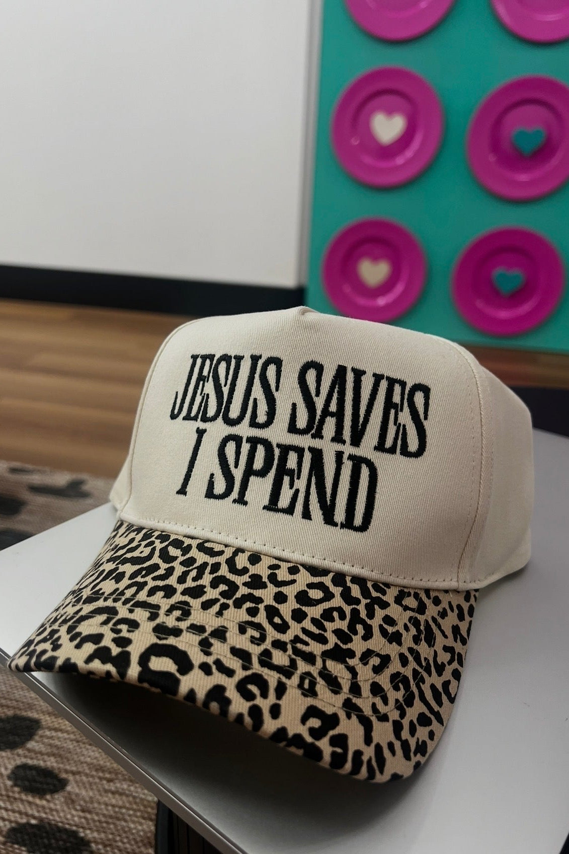 Cap with 'Jesus Saves I Spend' text on a surface with a colorful background