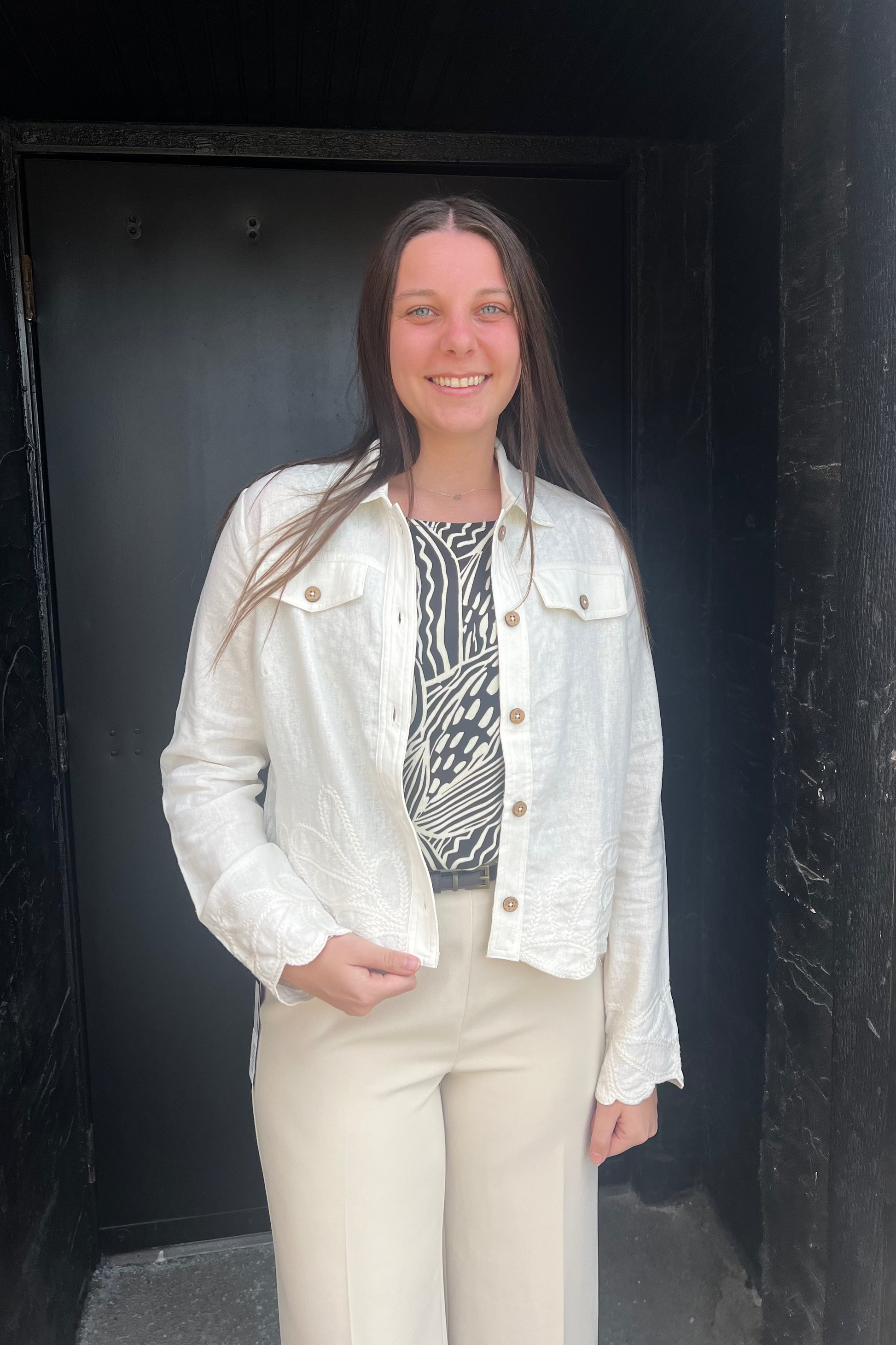 Person wearing a white jacket and patterned top standing against a dark background