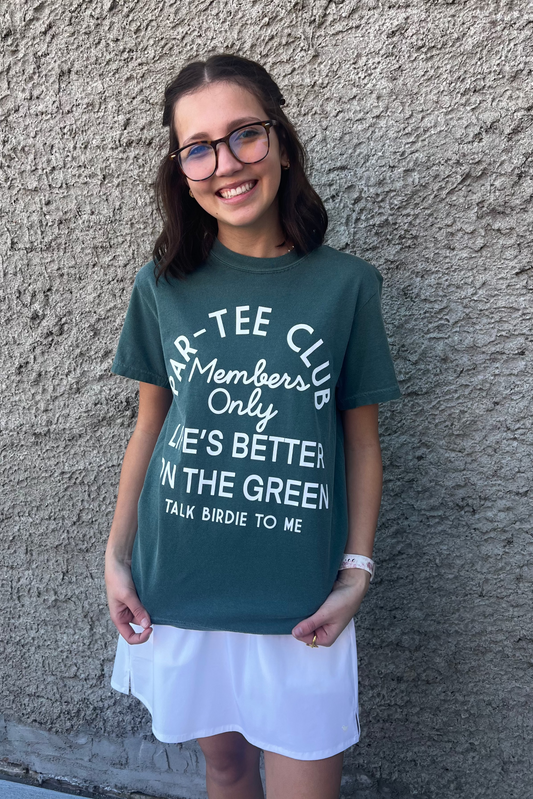 Person wearing a green t-shirt with text standing against a gray wall