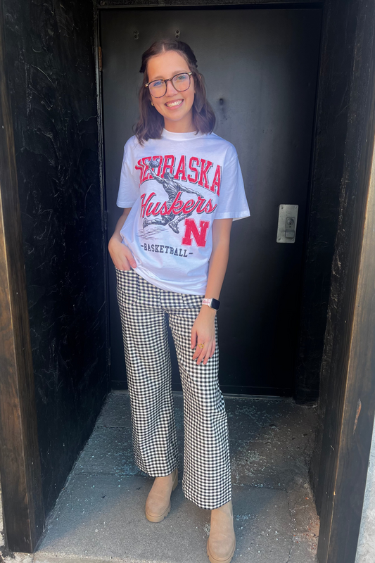 Person wearing a Nebraska Huskers t-shirt and checkered pants standing in a doorway.
