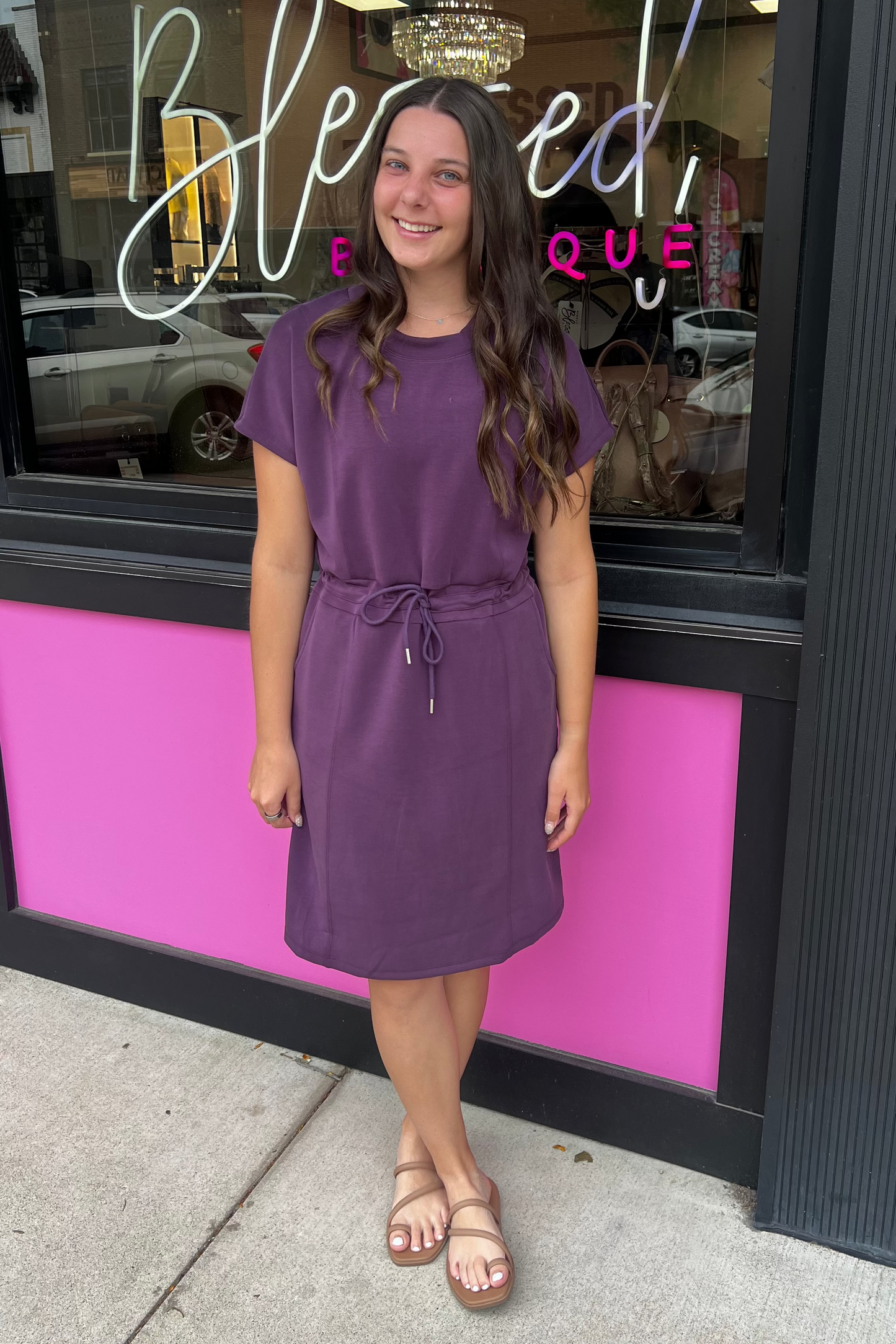 Woman in a purple dress standing in front of a store with a pink and black exterior.