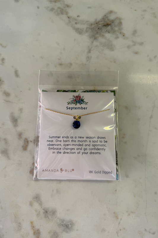 Necklace with a blue pendant on a branded card, displayed on a marble surface.