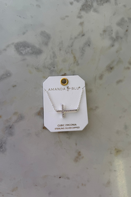 Silver necklace with cross pendant on a branded card, placed on a marble surface.
