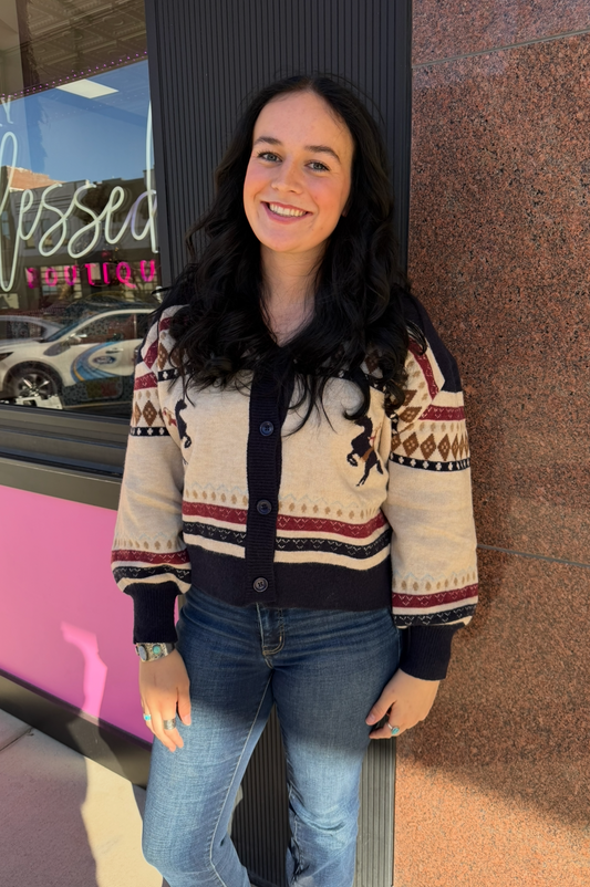 Woman wearing a patterned sweater and jeans standing against a colorful wall.
