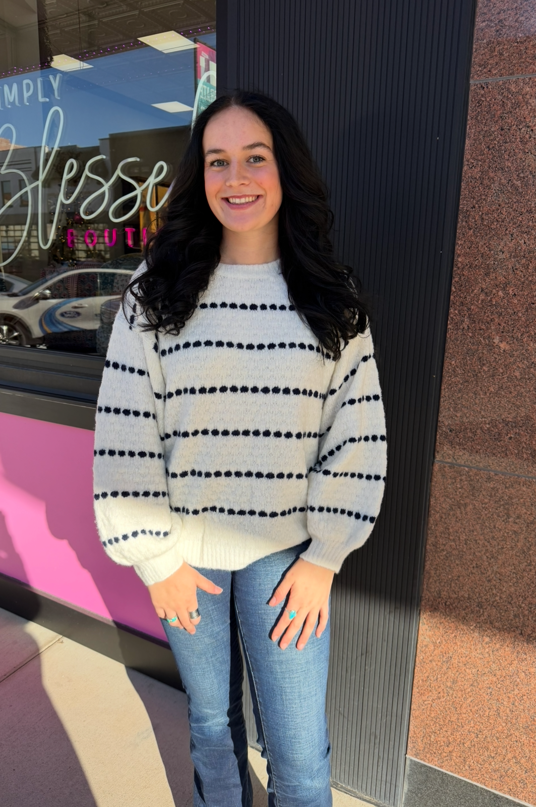 Person wearing a striped sweater and jeans standing in front of a store entrance.