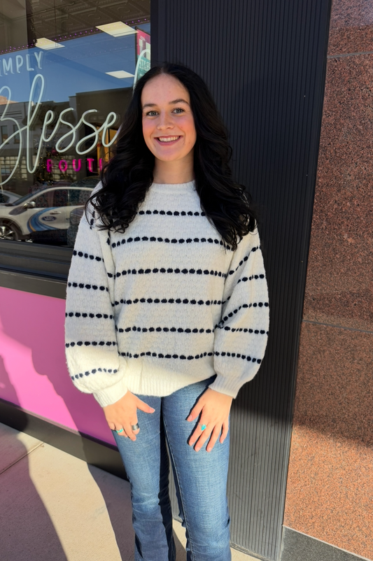 Person wearing a striped sweater and jeans standing in front of a store entrance.