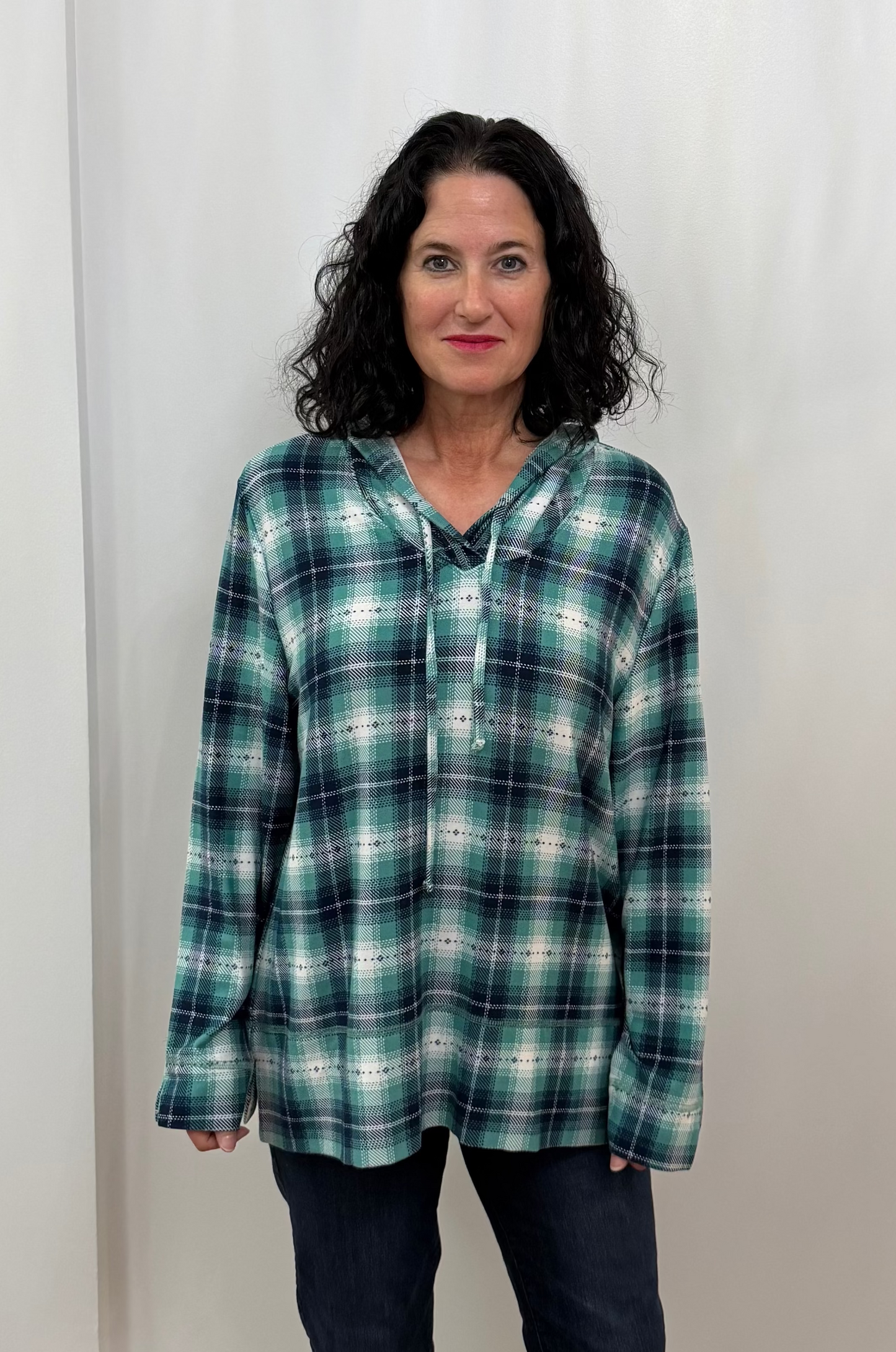 Woman wearing a plaid hoodie and dark pants against a plain background