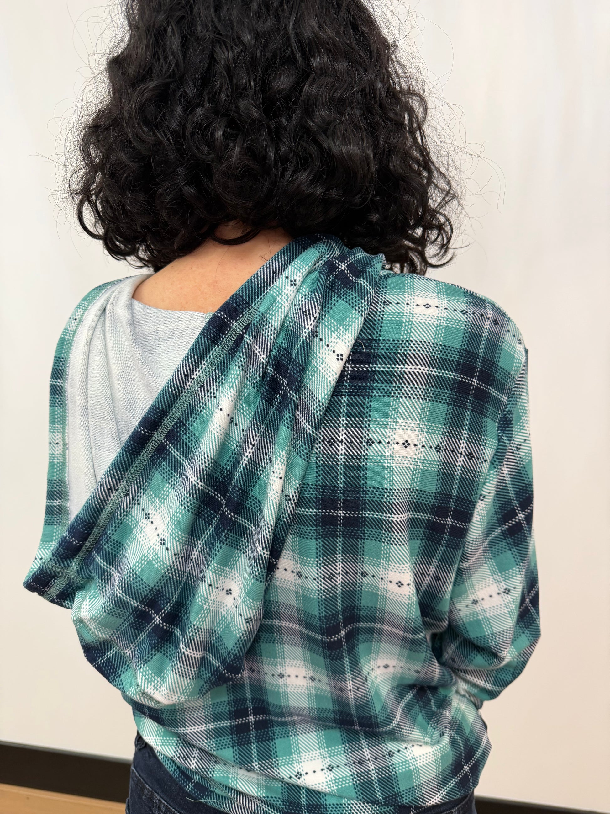 Person wearing a green and blue plaid shawl over shoulders against a plain background