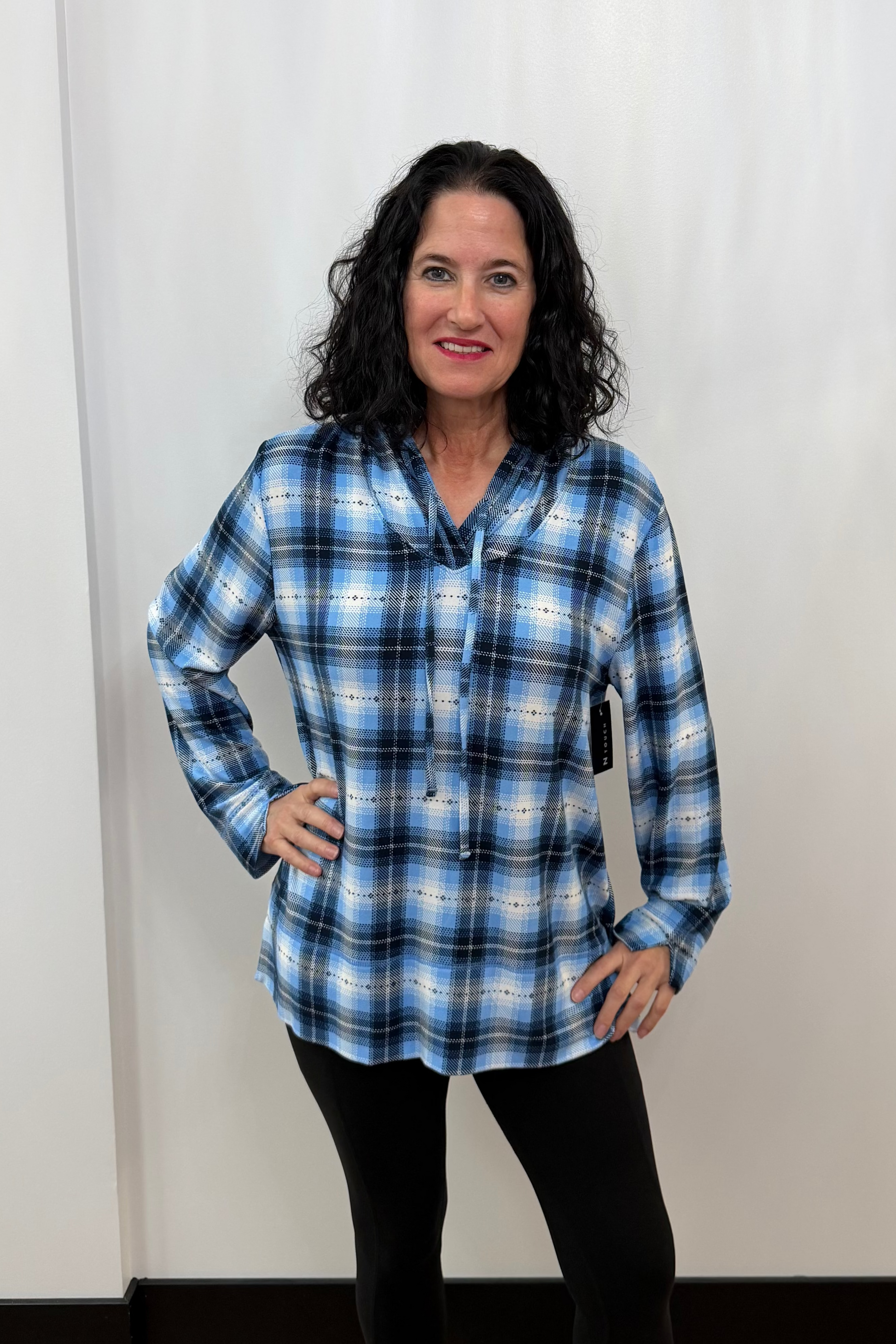 Woman wearing a blue plaid shirt standing against a white curtain.