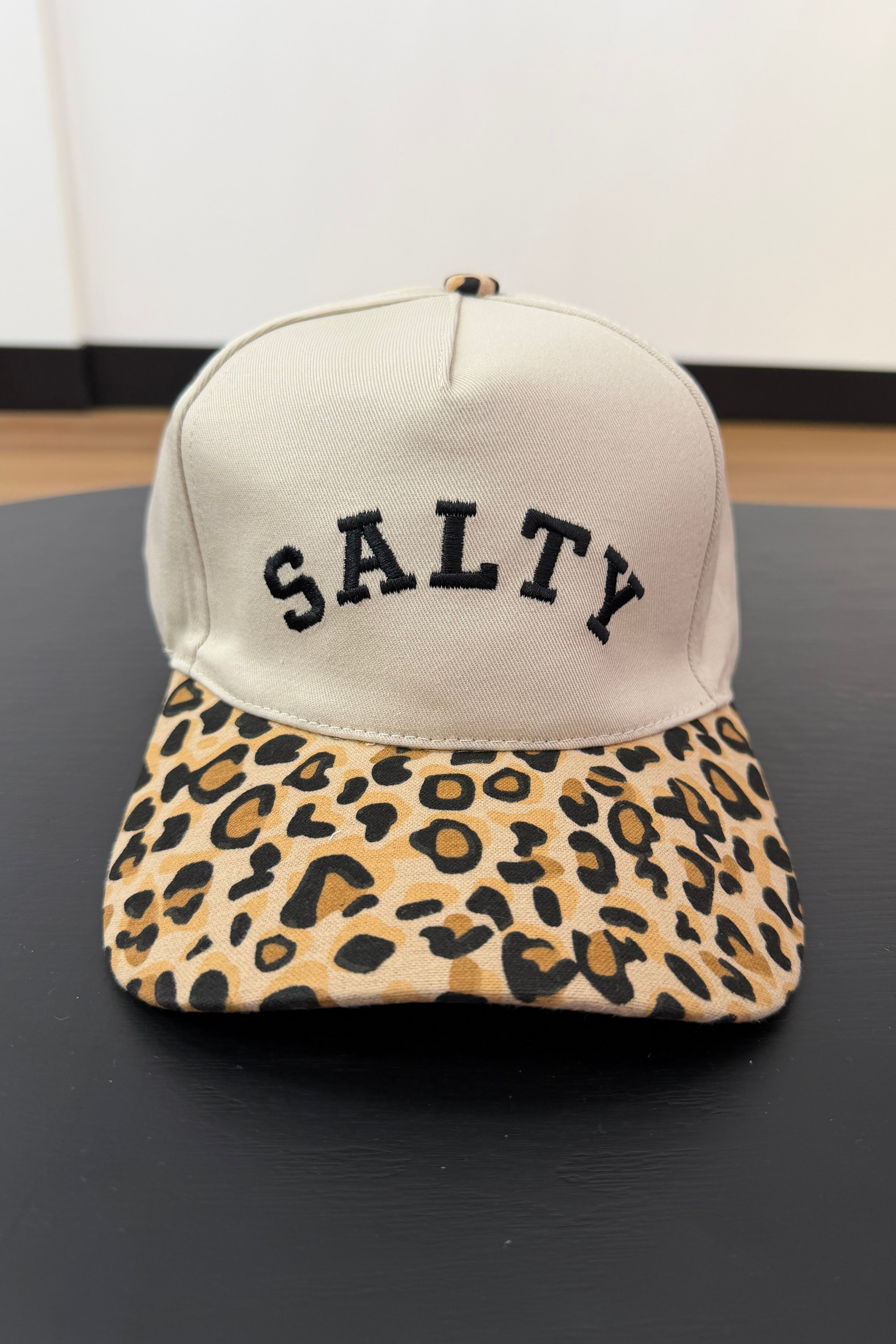 Cap with 'SALTY' text and leopard print brim on a black surface
