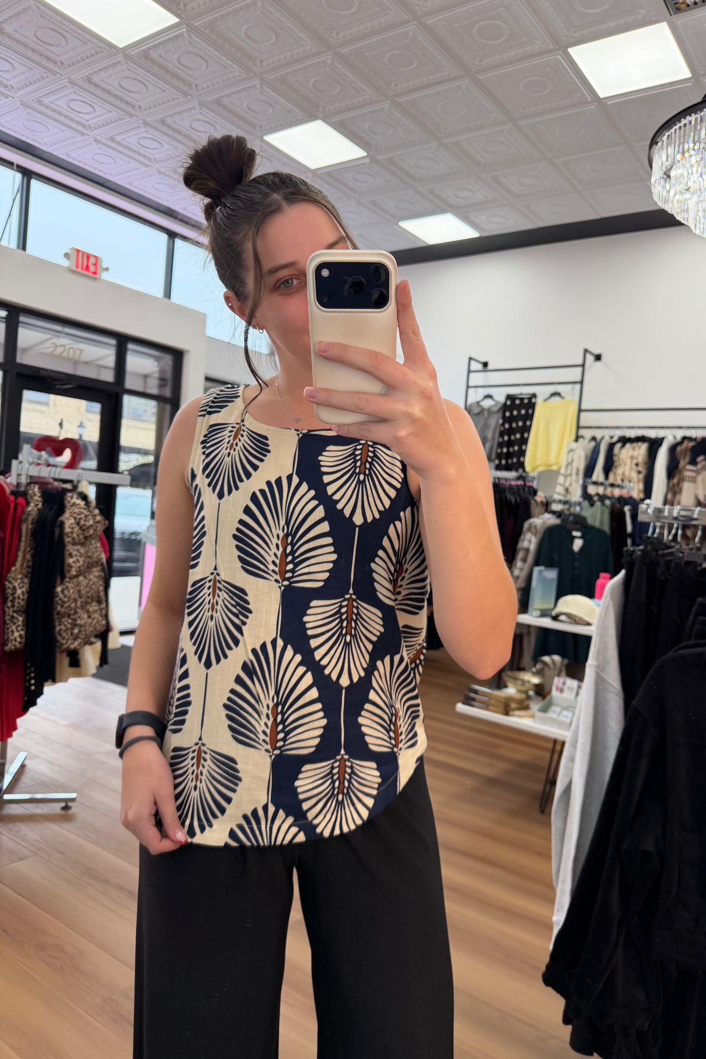 Woman taking a mirror selfie wearing a patterned top in a clothing store.