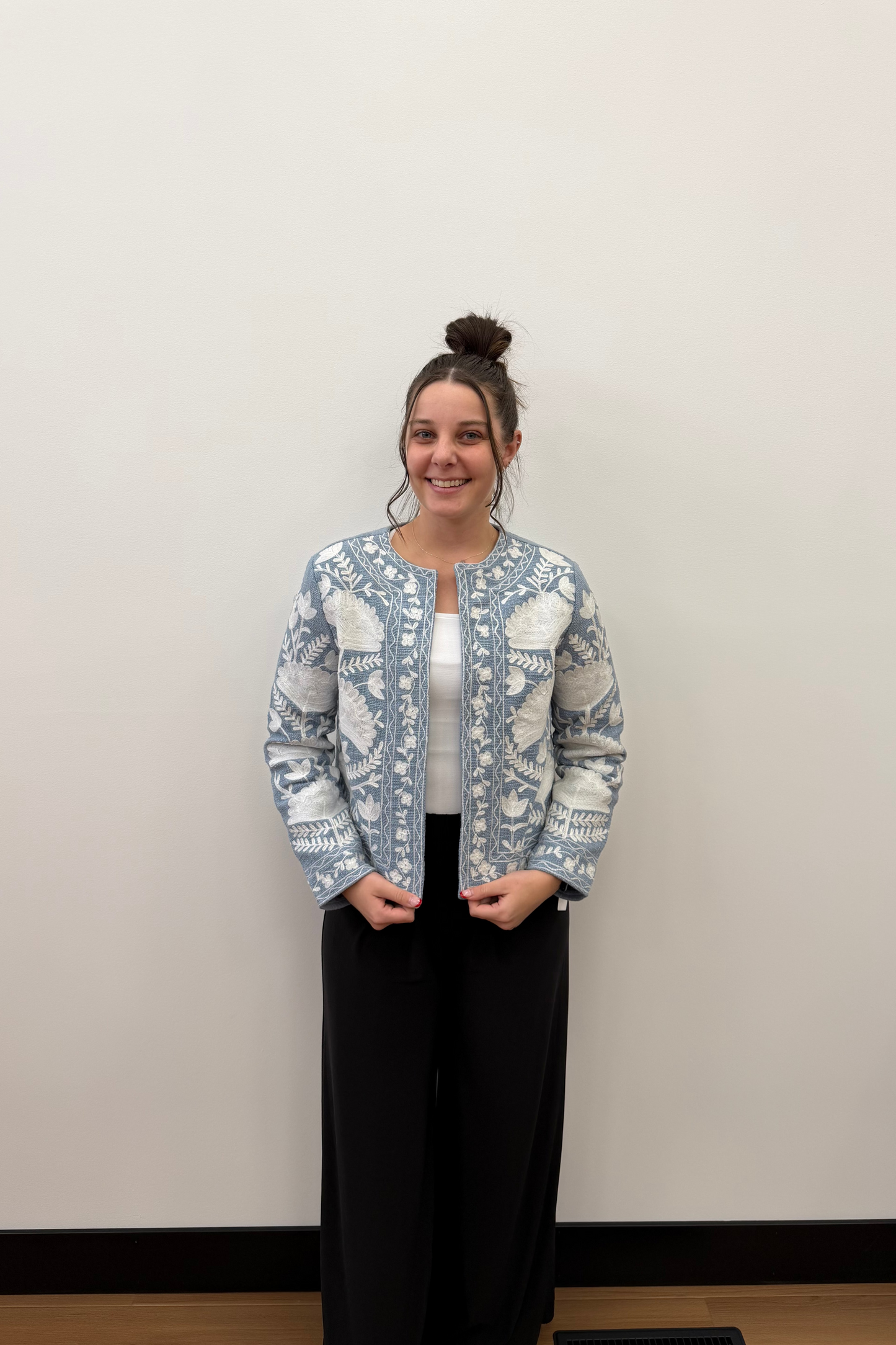 Person wearing a patterned blue jacket and black pants against a plain background