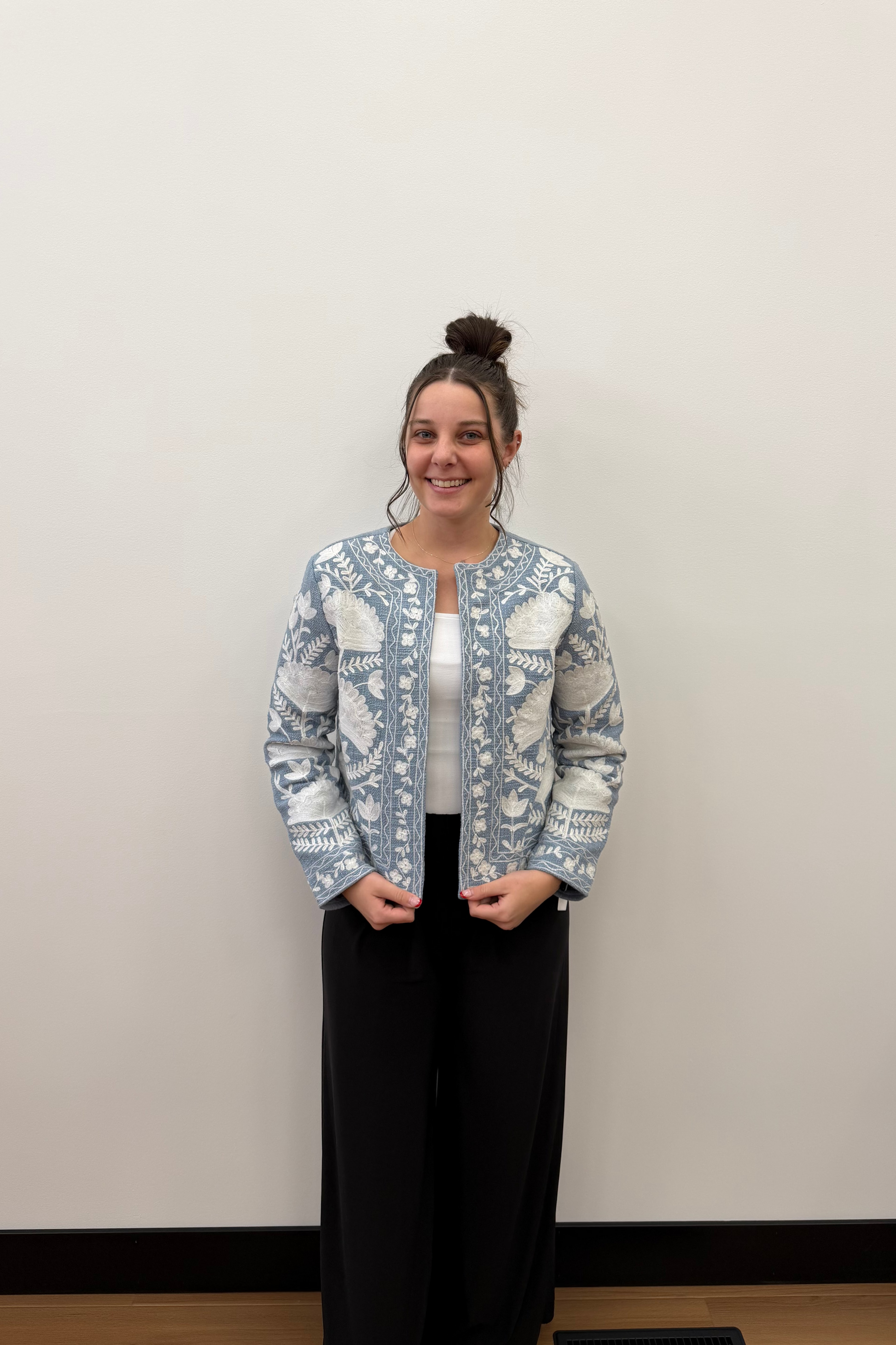Person wearing a patterned blue jacket and black pants against a plain background