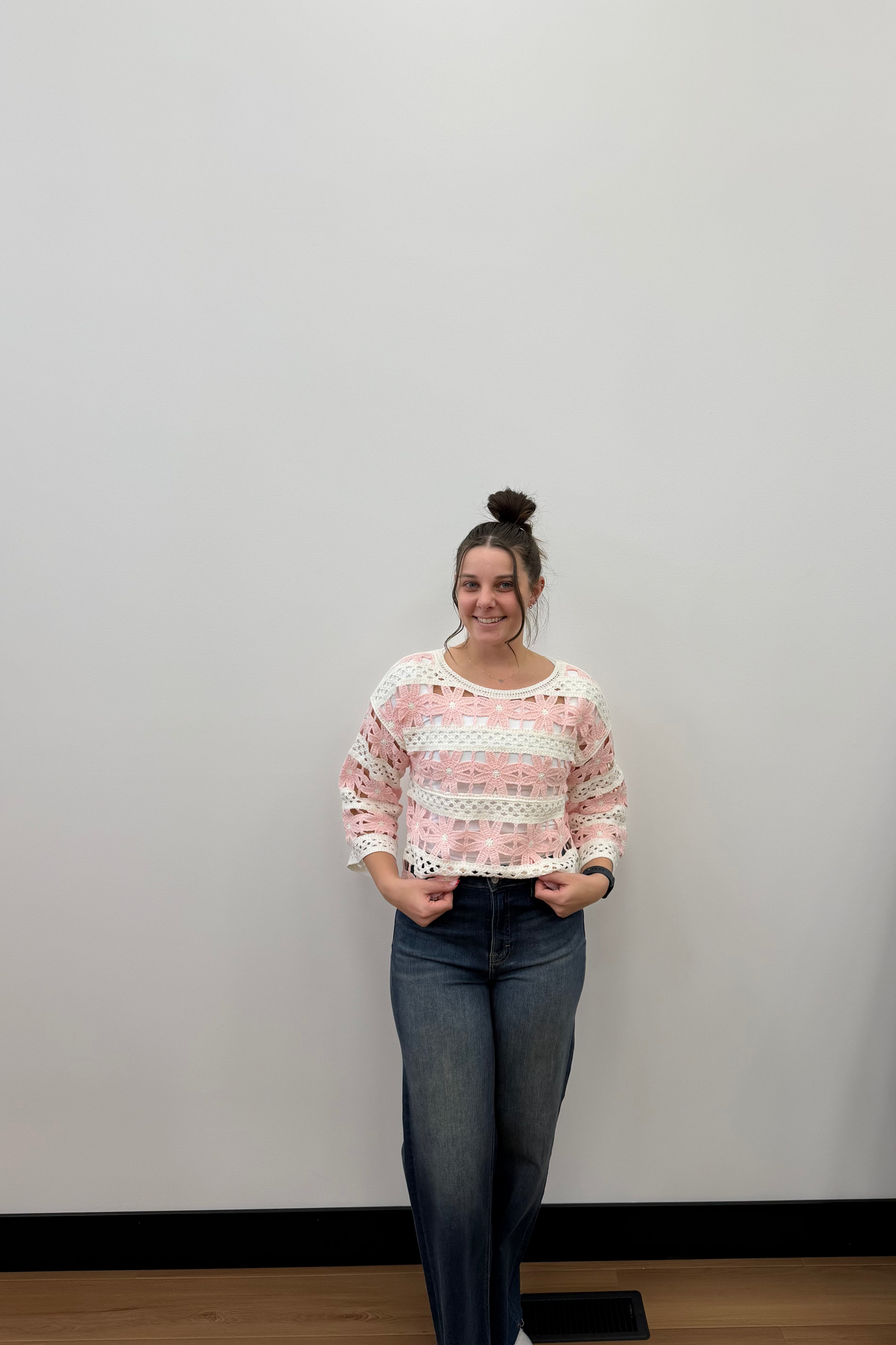 Woman wearing a pink and white patterned sweater and blue jeans standing against a plain wall.