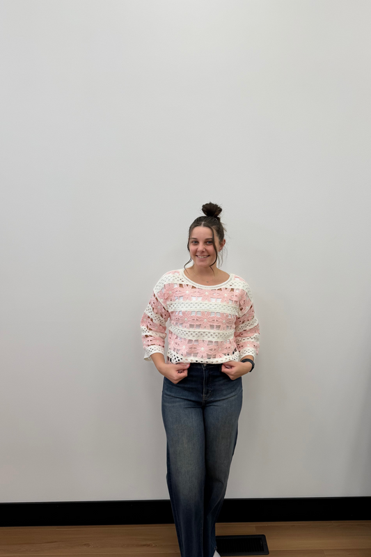 Woman wearing a pink and white patterned sweater and blue jeans standing against a plain wall.