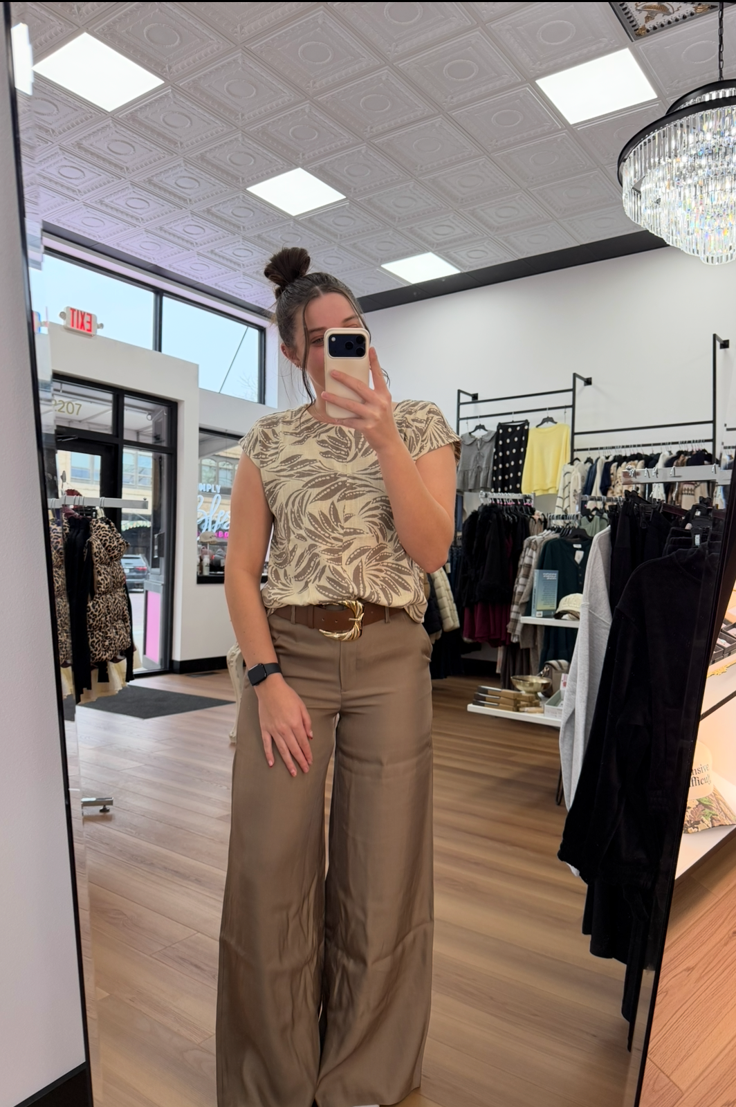Person taking a mirror selfie in a store wearing a floral top and beige pants.