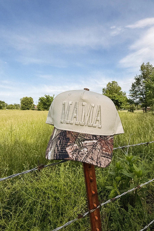 Two caps, one beige and one camouflage, on a fence post with a grassy field and blue sky in the background.