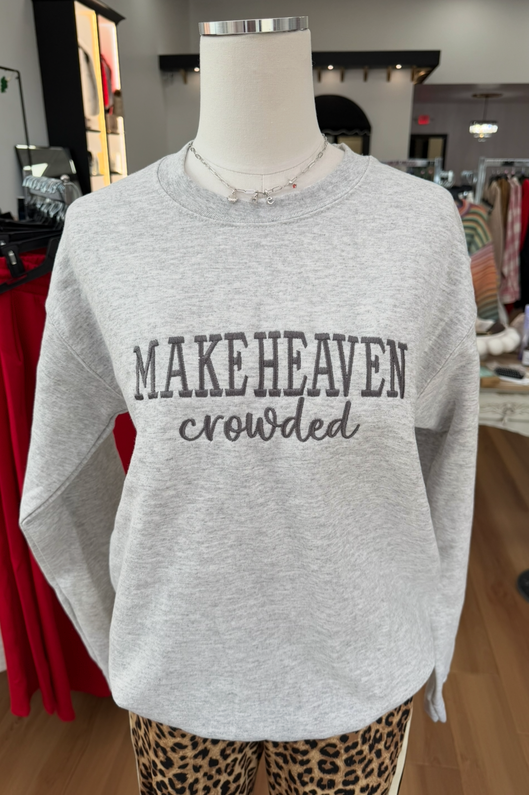 Gray sweatshirt with 'MAKEHEAVEN crowded' text on a mannequin in a store setting.