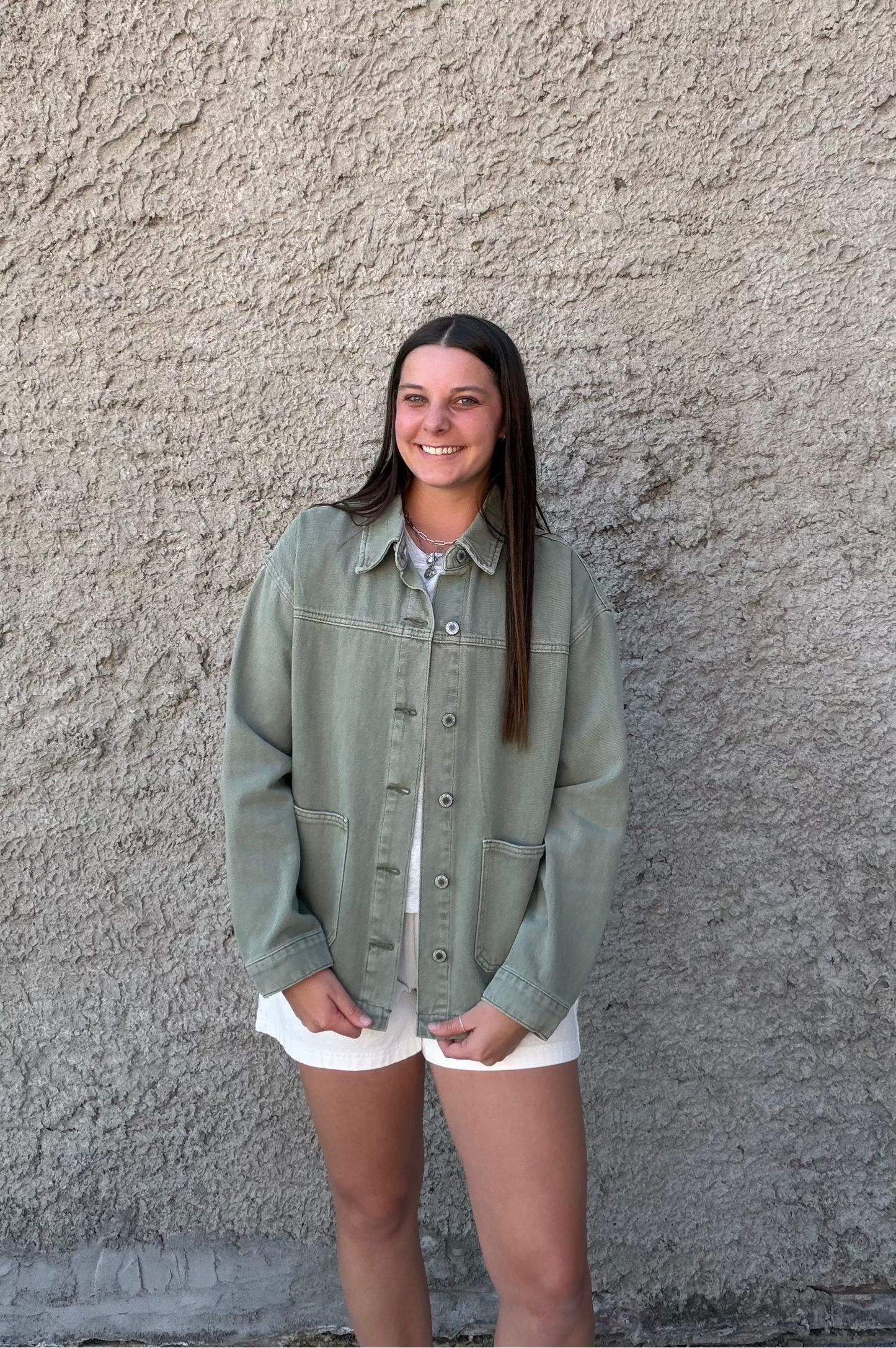 Woman wearing a green jacket standing against a textured wall